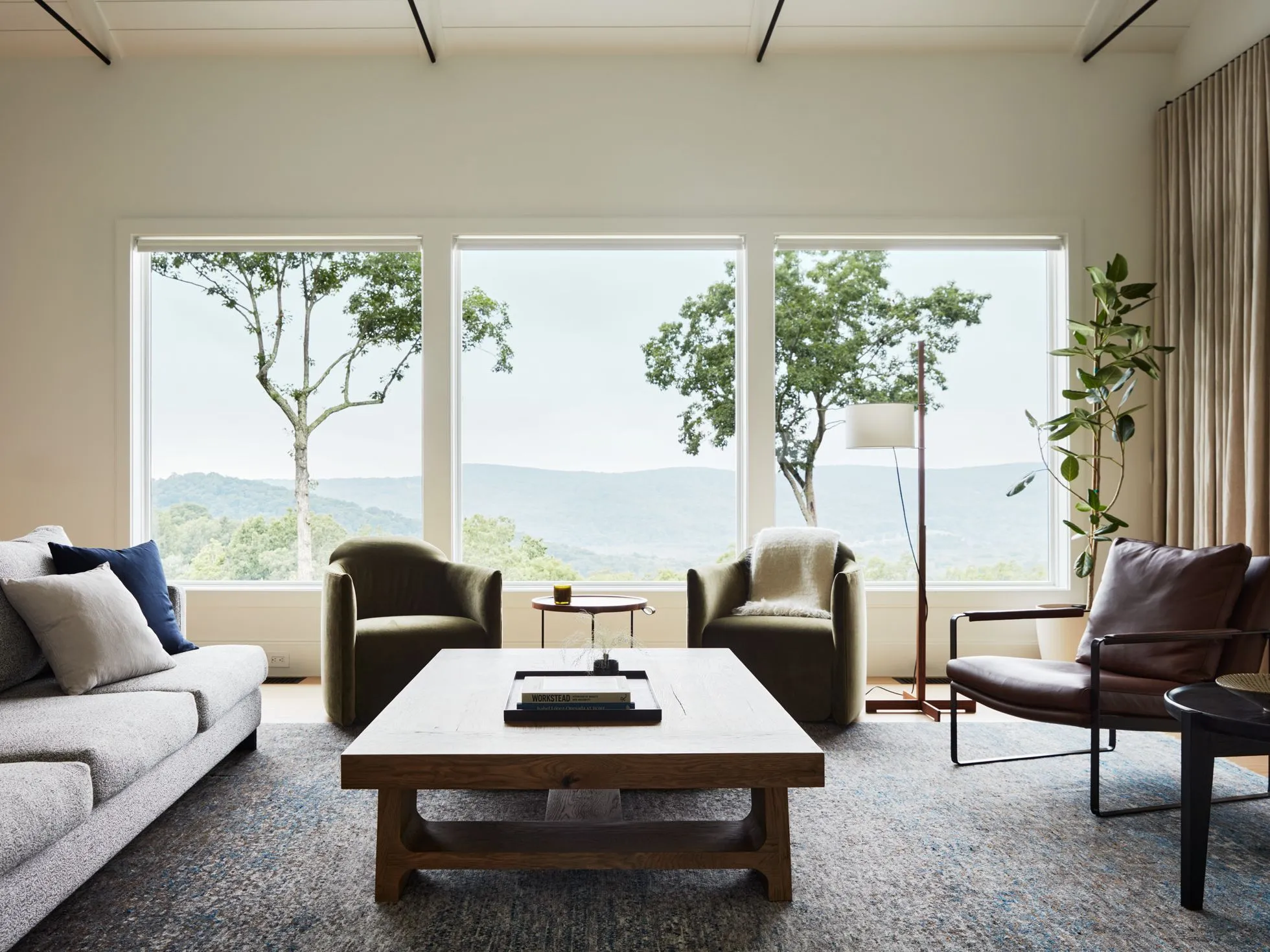 Double-height villa living room in Whitefield Bengaluru with a low sectional sofa, travertine flooring and tall sheer-draped windows